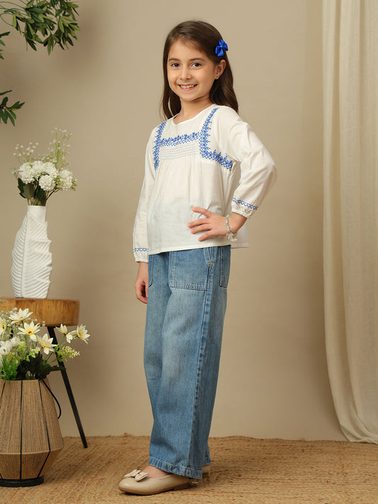 Girls white cotton top with blue embroidery, smocked yoke, round neckline and full sleeves.