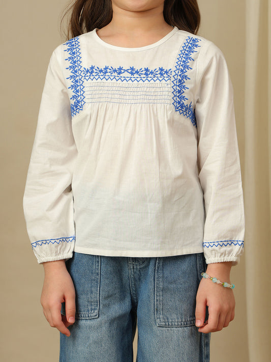 Girls white cotton top with blue embroidery, smocked yoke, round neckline and full sleeves.
