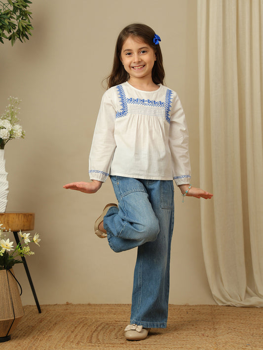 Girls white cotton top with blue embroidery, smocked yoke, round neckline and full sleeves.
